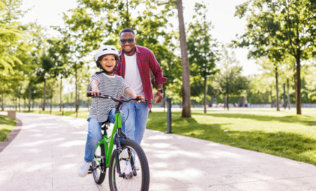 Happy african american family father teaches boy son to ride bike in park in natureの写真素材