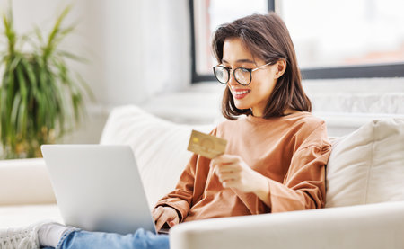 young cheerful woman is engaged in online shopping side on sofa with laptop and bank card at homeの写真素材