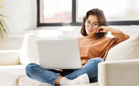 beautiful young girl woman laptop while sitting on sofa at homeの写真素材
