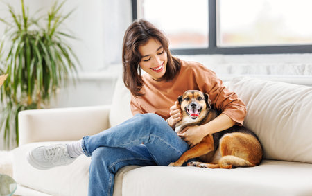 happy cheerful woman hugging her beloved pet dog at home on the couchの写真素材
