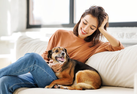 happy cheerful woman hugging her beloved pet dog at home on the couchの写真素材