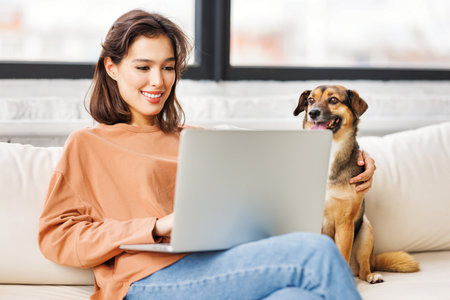 happy young female freelancer working on laptop remotely from home together with pet dogの写真素材