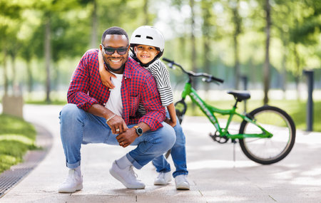 Happy african american family father teaches boy son to ride bike in park in natureの写真素材