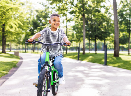happy african american boy riding bike in park in summerの写真素材