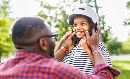Happy family: father puts on son helmet for safe cycling in park in natureの写真素材
