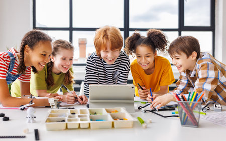 Positive kids pupils schoolchildren happy smiling and looking at tablet screen during celebrate together successful completion of collective school work in a light classroomの写真素材