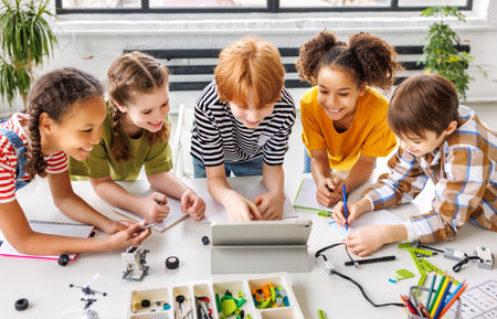Positive kids pupils schoolchildren happy smiling and looking at tablet screen during study scheme of assembly of robots duringcollective school work in light classroomの写真素材