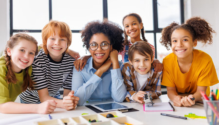 Happy woman teacher in casual clothes and glasses and cheerful kids students looking at camera during lesson in sunlit classroomの写真素材