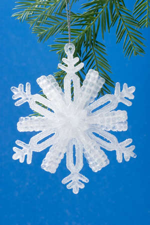 Snowflake made from crystal on small branch of Christmas tree and sky colored backgroundの写真素材