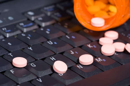 Notebook keyboard covered by pills pouring out of a prescription bottleの写真素材