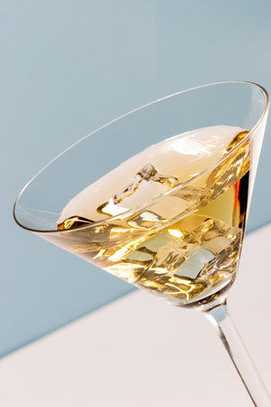 Martini glass full of cocktail with one cube of ice on the bottom over aqua paper backgroundの写真素材