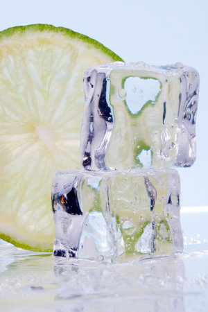 Two stacked ice cubes melted in water and slice of lime on reflection surface ready to be added to a cocktailの写真素材