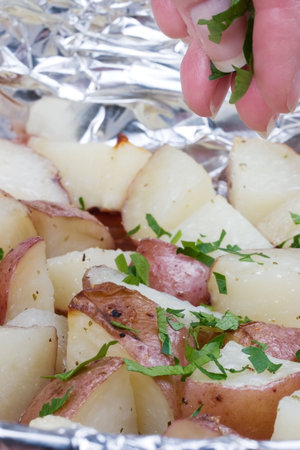 Foil tray full of ready to eat roasted potato sprinkled by parsleysの写真素材