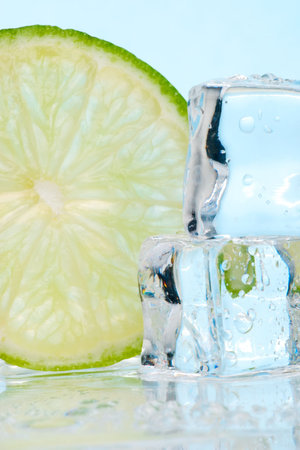 Two stacked ice cubes melted in water and slice of lime on reflection surface ready to be added to a cocktailの写真素材