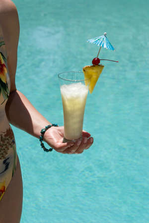 Woman on swimming pool side with glass of Pina Colada cocktail  in her handの写真素材