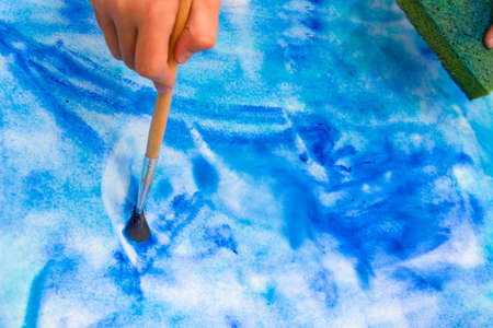 Closeup of hand with brush creating wet on wet watercolor blue colored painting の写真素材