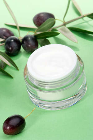 Closeup of jar of moisturizing face cream and olive twig on green toned background の写真素材