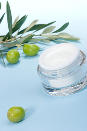Closeup of jar of moisturizing face cream and olive twig on aqua toned background の写真素材