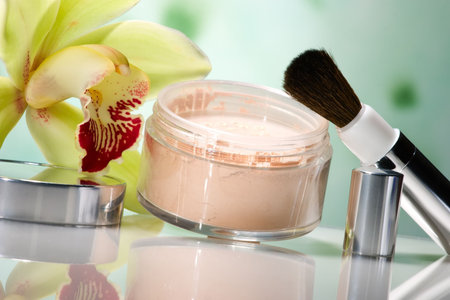 Closeup of container of opened face powder, brush and blooming yellow orchid floweron on reflected...