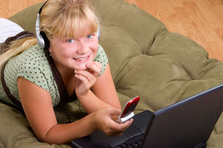 Blond cute teenager girl on sofa with laptop and a cell phoneの写真素材