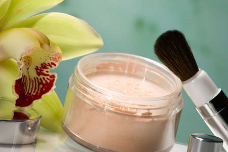 Closeup of container of opened face powder, brush and blooming yellow orchid flower on reflected surfaceの写真素材