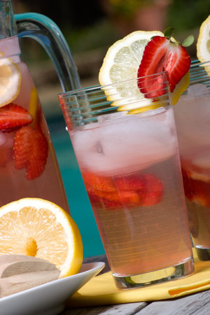 Closeup of two glasses of home made iced cold pink strawberry lemonade and pitcher on hot summer on...