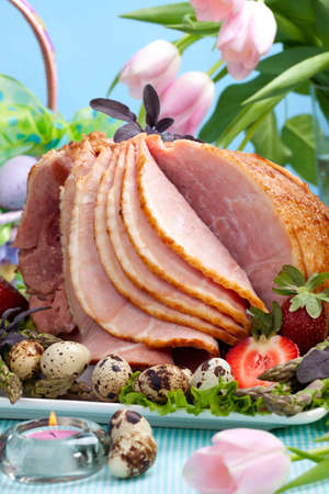Honey ham on Easter table with quail eggs, tulips and decorationの写真素材
