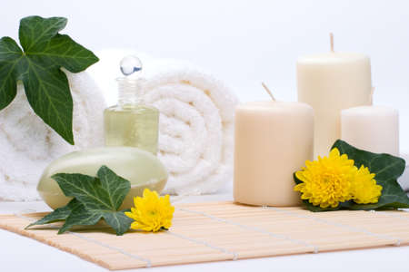 Spa set - Chrysanthemums flowers, body oils, organic soap on bamboo mat and towels with ivy leaves over white background best suited for relaxing and health commercialsの写真素材