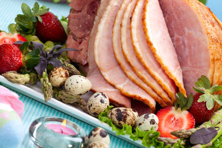 Honey ham on Easter table with quail eggs, tulips and decorationの写真素材