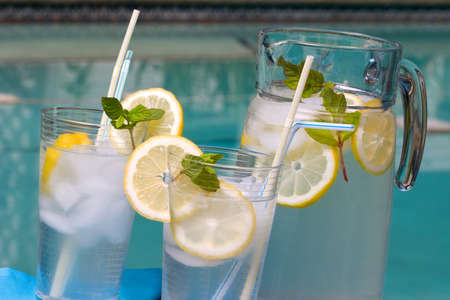 Two glasses of home made iced cold lemonade and pitcher on hot summer on edge of swimming pool. の写真素材