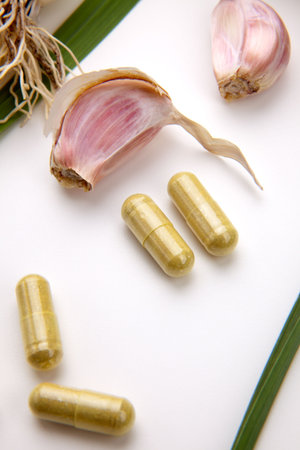 Closeup of garlic extract pills and fresh garlic leaves and cloves best suited for health, anti-cholesterol and alternative medicine adsの写真素材