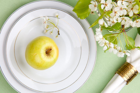 Single apple on plates in spring table settings with apple tree flowersの写真素材