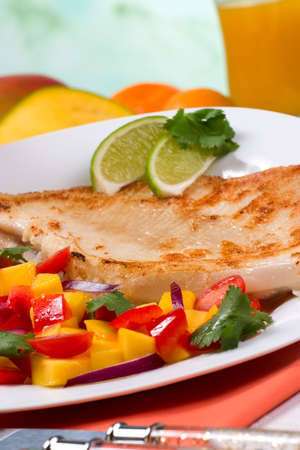 Closeup of fried skate (ray) with mango, cherry tomato and red onion salsa. Fresh fruits and glass of juice.の写真素材