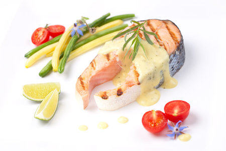 Closeup of delicious grilled salmon steak with tarragon sauce garnished with beans and cherry tomatoes.の写真素材