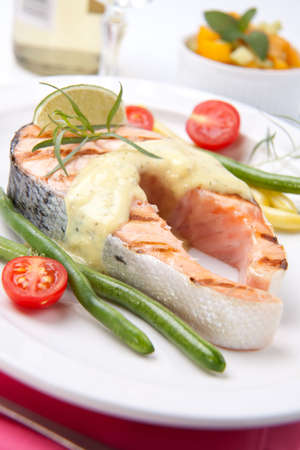 Closeup of delicious grilled salmon steak with tarragon sauce garnished with beans and cherry tomatoes.の写真素材