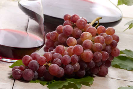 Glass of red wine, decanter and fresh cut black wine grape bunch.の写真素材