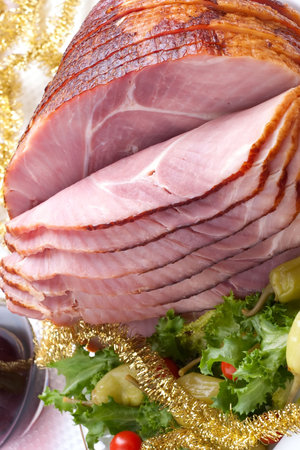 Holiday table setting with delicious whole baked sliced ham, marinated peppers, cherry tomatoes, vegetable salad and glasses of red wine. Christmas decoration, candles, ornaments around.の写真素材