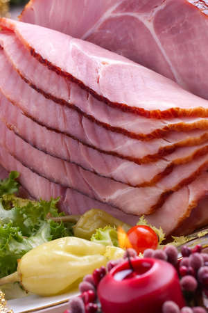 Holiday table setting with delicious whole baked sliced ham, marinated peppers, cherry tomatoes, vegetable salad and glasses of red wine. Christmas decoration, candles, ornaments around.の写真素材