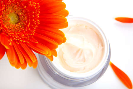 Closeup of jar of moisturizing face cream surrounded by orange gerbera flowersの写真素材