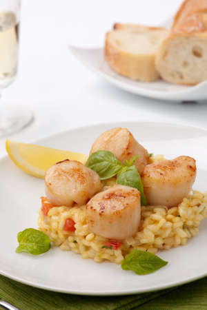 Plate of Scallops Risotto garnished with fresh basil, glass of white wine and bread.の写真素材