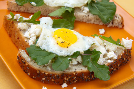 Closeup of delicious open-face sandwiches with feta cheese, arugula, and fried quail eggs.