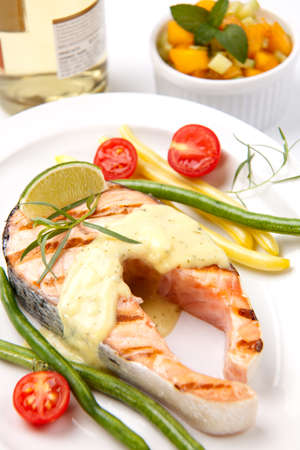 Closeup of delicious grilled salmon steak with tarragon sauce garnished with beans and cherry tomatoes.の写真素材