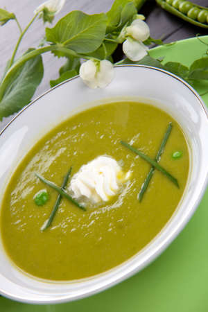 Bowl of pea soup garnished with chives and cream. Sprig of flowering pea and cracked pea pods.の写真素材