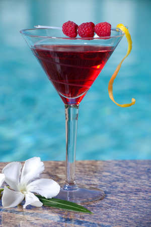 Glass of Raspberry Cosmopolitan cocktail on swimming pool side garnished with fresh raspberriesの写真素材
