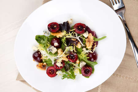 Green salad with cherries, walnuts and blue cheese. Fresh cherries around. Saucer with vinaigrette.の写真素材