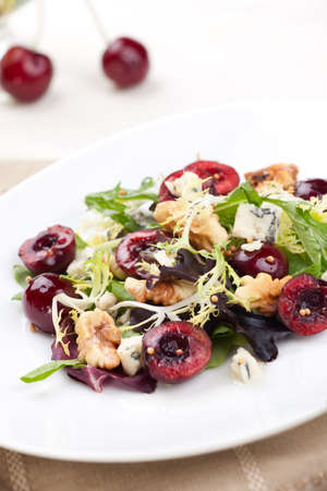 Green salad with cherries, walnuts and blue cheese. Fresh cherries around. Saucer with vinaigrette.の写真素材