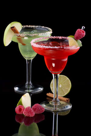 Apple and Raspberry margaritas in chilled glass over black background on reflection surface, garnished slice of green apple, fresh raspberries, slice of lime and cinnamon stick. Most popular cocktails series.の写真素材