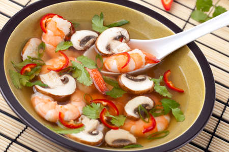 Closeup of a bowl of hot-and-sour prawn soup with mushrooms, prawns, chili pepper and cilantro.の写真素材