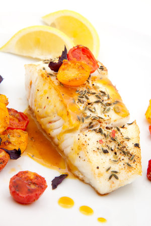 Pan fried halibut garnished with fennel seeds and spicy mustard sauce, served with fried cherry tomatoes salad with purple basilの写真素材