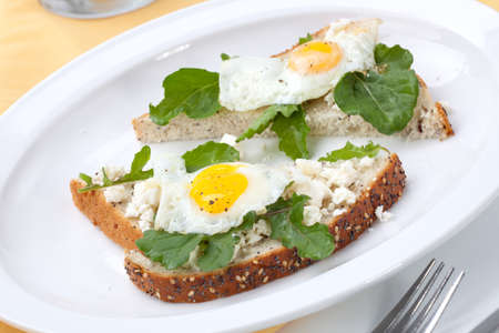Closeup of delicious open-face sandwiches with feta cheese, arugula, and fried quail eggs.の写真素材
